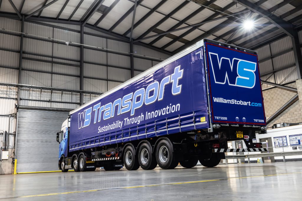 Blue articulated lorry with trailer parked inside warehouse, industrial building interior visible.